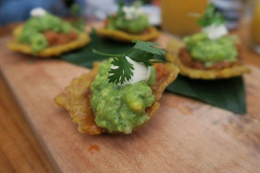 A food item with a green topping, possibly guacamole, on a crispy base, garnished with a leaf. 3