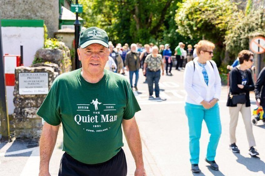 A man in a green shirt with a logo, walking on a street with pedestrians in the background. 5