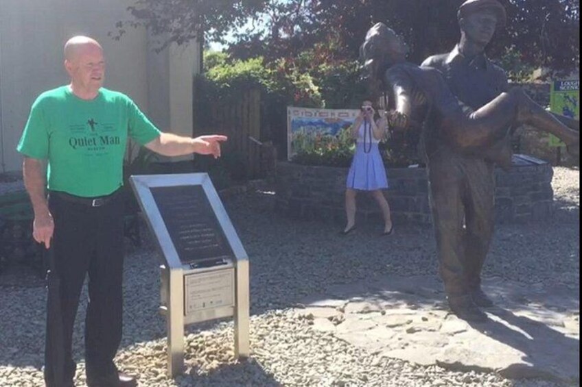 A man in a green shirt pointing at a signboard, a statue, and a woman in a blue dress taking a photo. 2