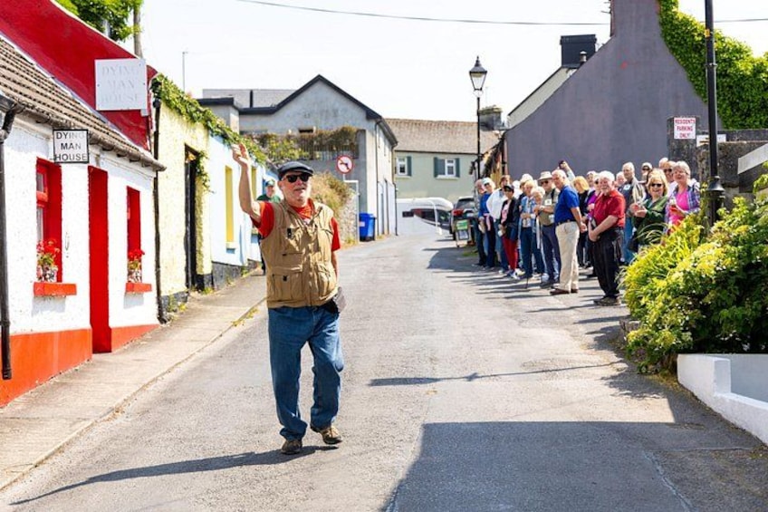 A street with a group of people standing in line, a man walking down the road, and buildings with red and white facades. 4