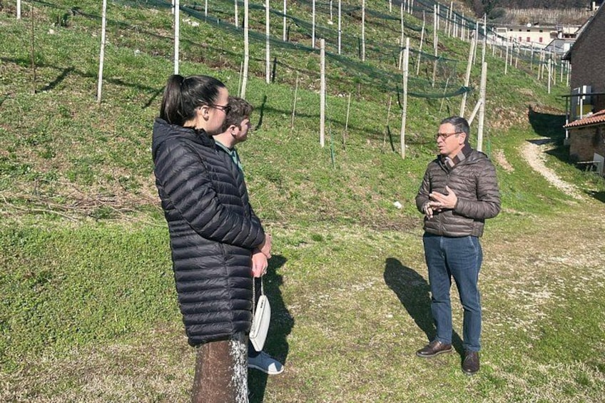 Drei Personen stehen auf einer grünen Böschung, ein Pfad führt bergauf, umgeben von viel Grün und einem Gebäude im Hintergrund. 2