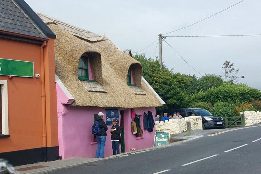 Un bâtiment rose avec un toit de chaume, une enseigne indiquant « The Sweeney's », et une voiture garée. 4