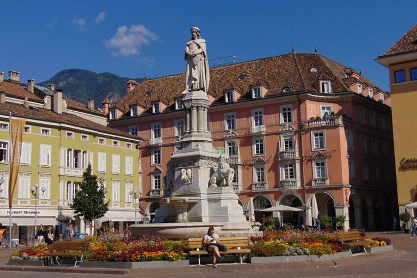 A statue in a square with colorful buildings and a mountain in the background. 1