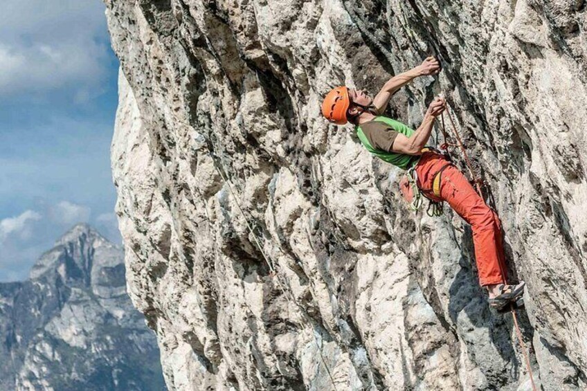 Una persona practica escalada en un risco escarpado y rocoso, con un paisaje montañoso de fondo. 2