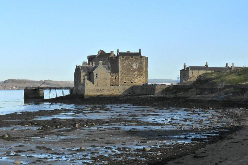 A historic stone castle by a rocky shoreline with a bridge leading to it. 3