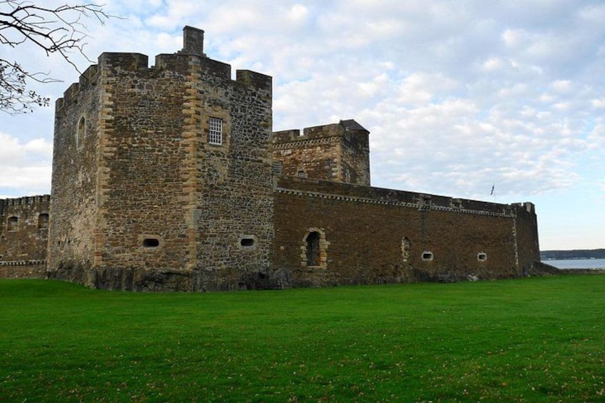 A historic stone castle with a large tower, surrounded by a grassy field and a body of water in the background. 2