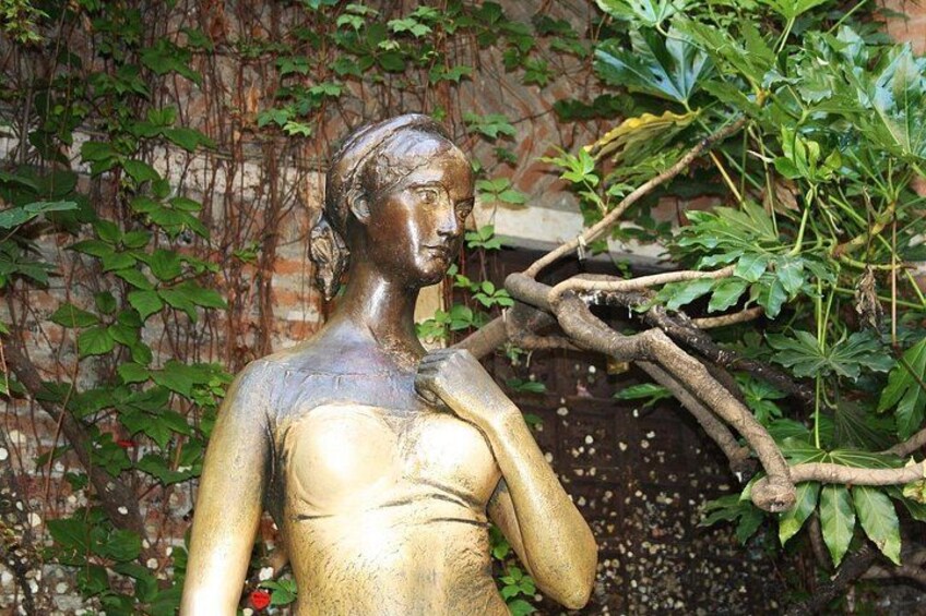 A bronze statue of a woman with a branch in her hand, set against a backdrop of ivy and a brick wall. 5