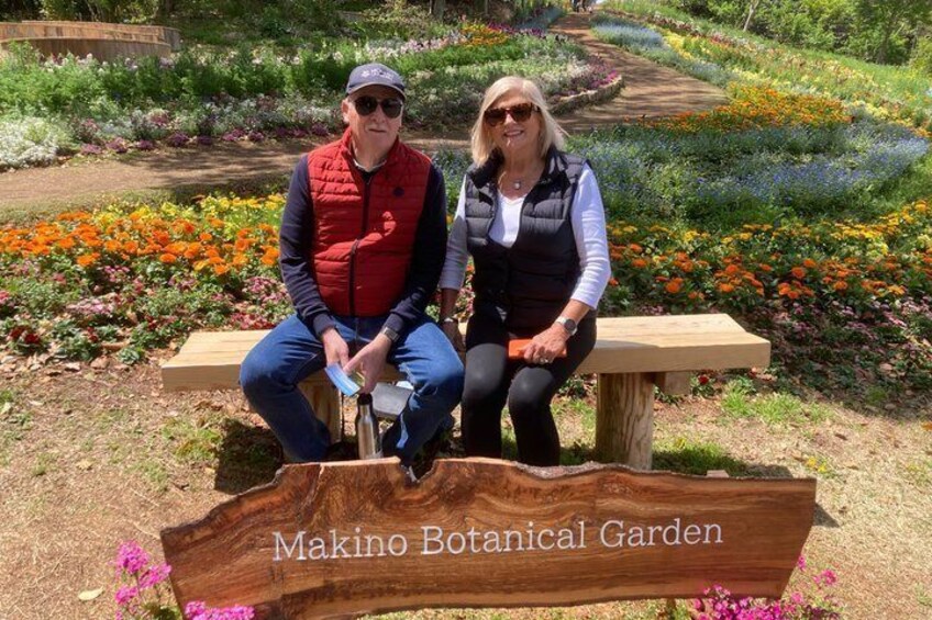 Two people sitting on a wooden bench in a botanical garden with a sign that reads 'Makino Botanical Garden.' 3