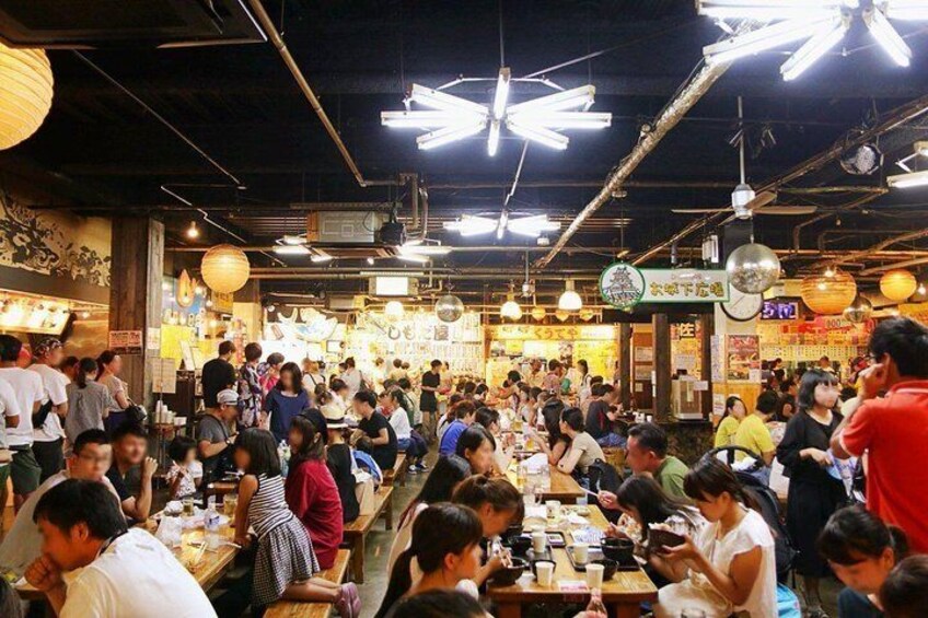 A crowded indoor market with people shopping and dining. 1