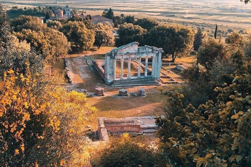 An ancient Greek temple surrounded by trees and fields. 2