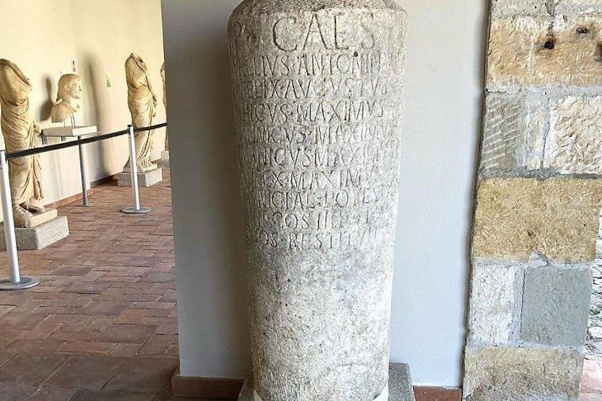 A stone column with inscriptions, surrounded by statues and a brick floor. 3