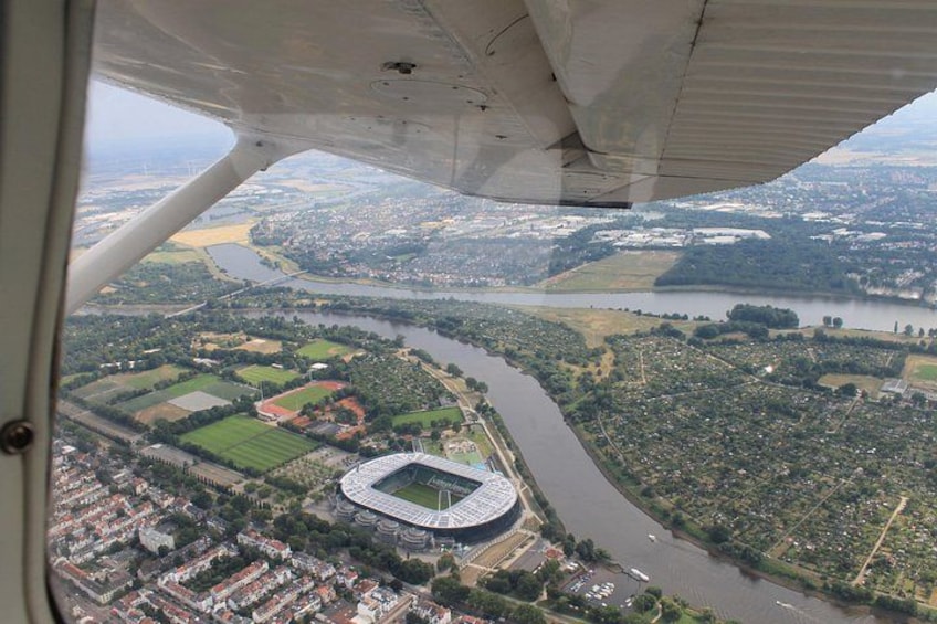 Ett flygbildsbild av en stad med en flod, en stadion och omgivande grönområden. 4
