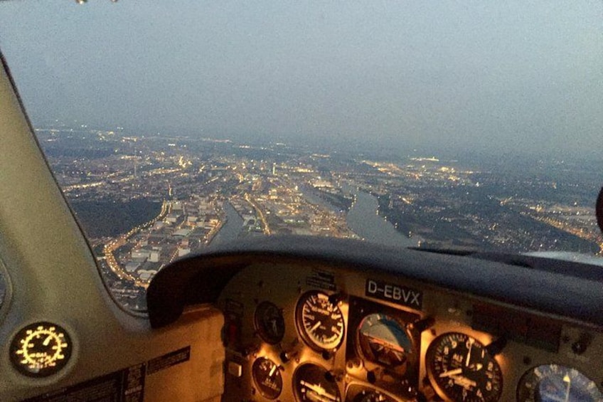 En vy från cockpit med flera mätinstrument och en stadsbild i bakgrunden. 5