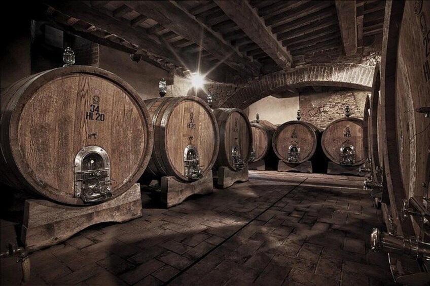Barricas de madera en una bodega tenuemente iluminada, con paredes de piedra y suelo de ladrillo. 2