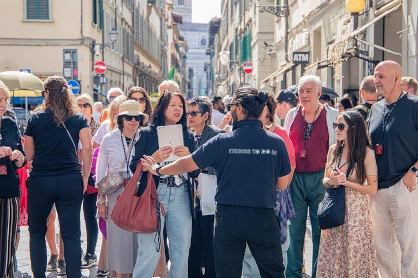Una strada affollata con persone che camminano e fermi, palazzi lungo la via e un cartello per un bancomat. 4