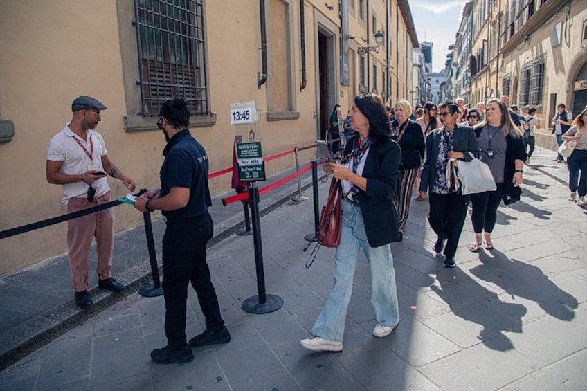 Una strada con persone in coda, un segnale che indica un limite di tempo e un edificio con grate alle finestre. 3