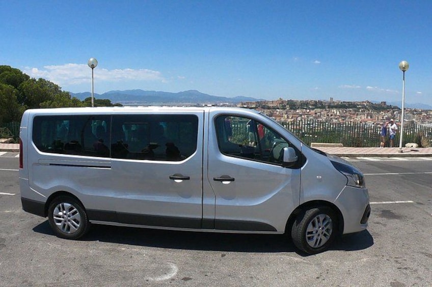 A silver van parked on a road with a cityscape and mountains in the background. 2