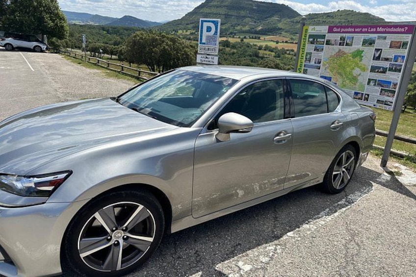 A silver car parked near a signboard with a map and text. 1