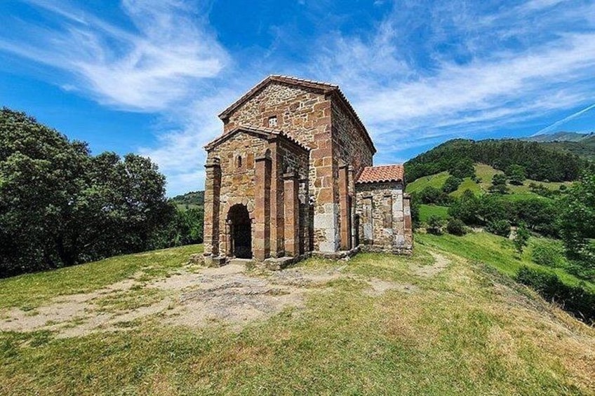 A stone building with a tiled roof, surrounded by green hills and trees. 2
