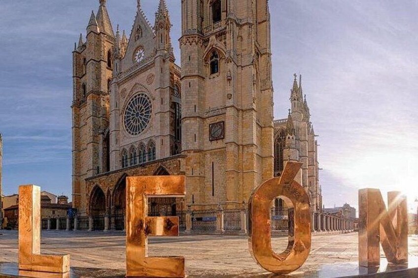 A historic cathedral with Gothic architecture, a large clock, and the word 'LEON' in the foreground. 3