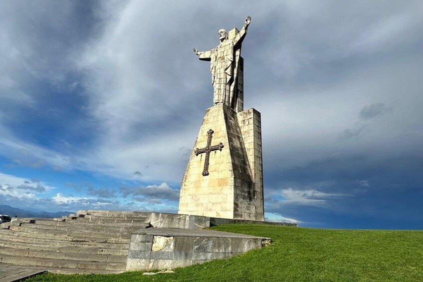 A large stone monument with a cross, a statue at the top, and a grassy area in the foreground. 5