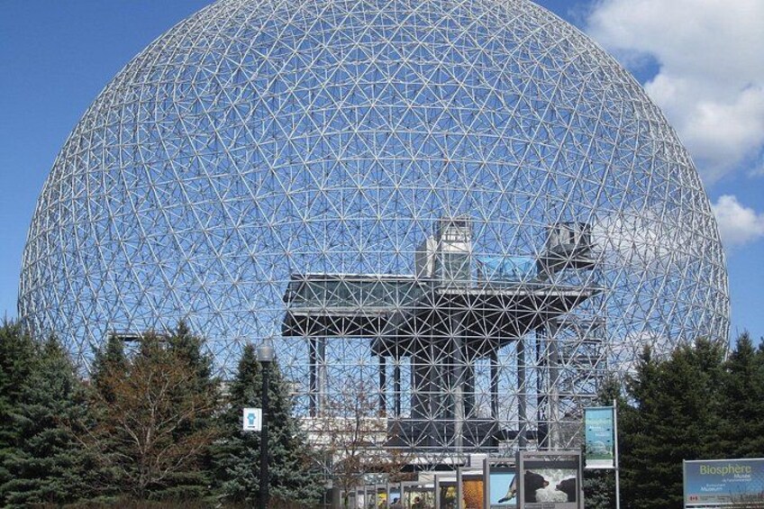 Una gran estructura en forma de geodésica con armazón metálico, rodeada de árboles y un cielo despejado. 2