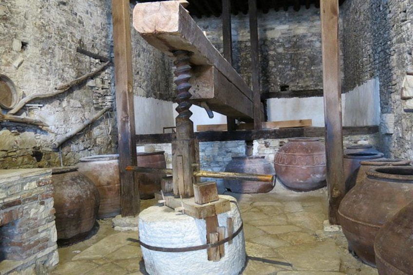 An old stone building with wooden beams, large clay pots, and a water wheel. 5