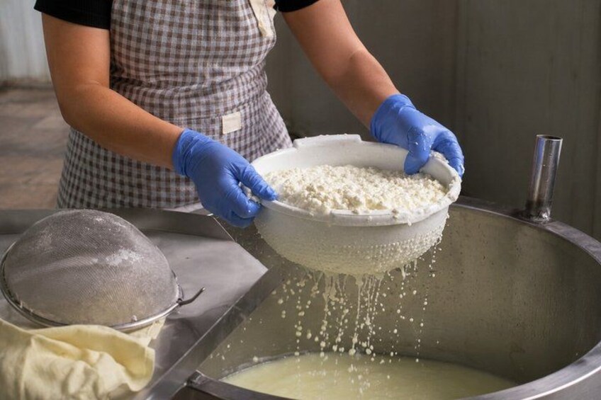 A person wearing gloves handling a bowl of white substance, possibly cheese, over a large metal container. 3