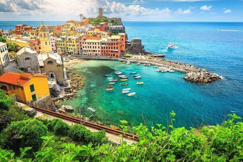 A coastal town with colorful buildings, a clear blue sea, boats, and a rocky breakwater. 5