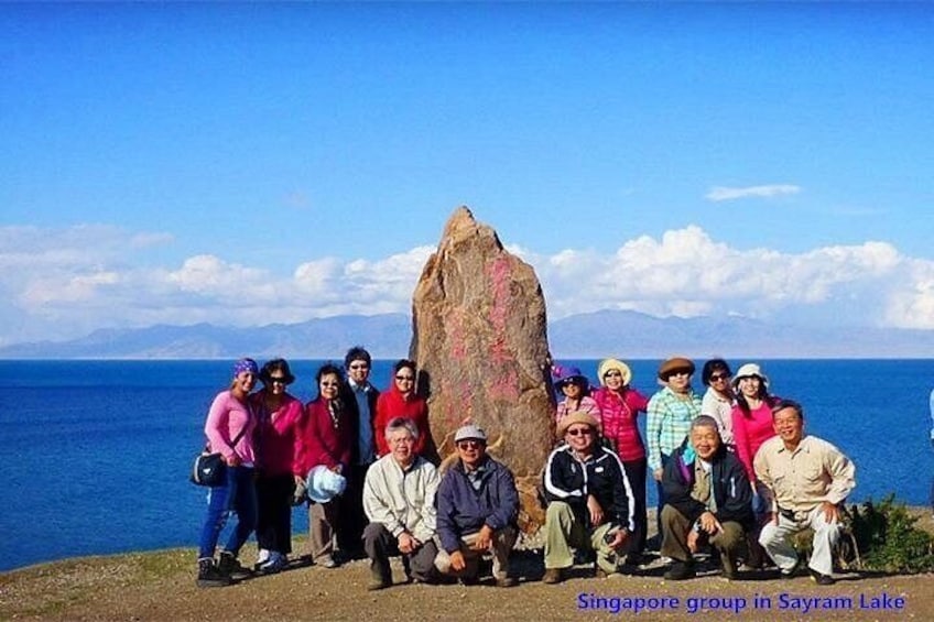 A group of people posing in Sayram Lake with a large rock formation in the background. 1
