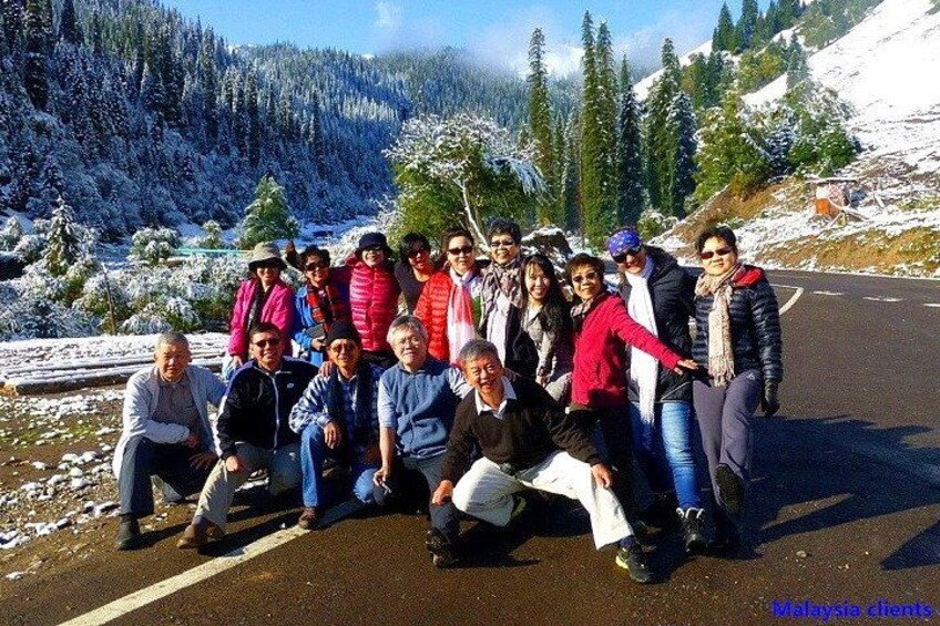 A group of people posing on a road with snow-covered trees and mountains in the background. 2