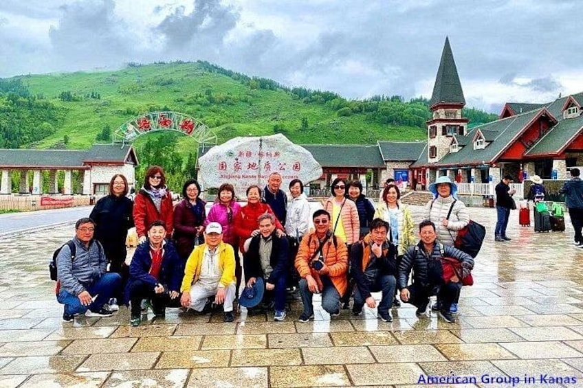 A group of people posing in front of a sign with Chinese characters, with a church and green hills in the background. 5
