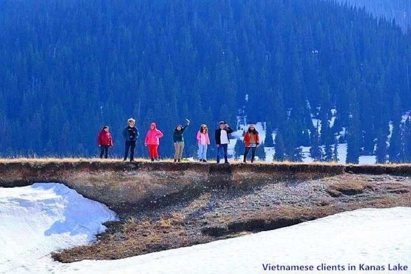 A group of people standing on a snowy slope with a forested mountain in the background. 1