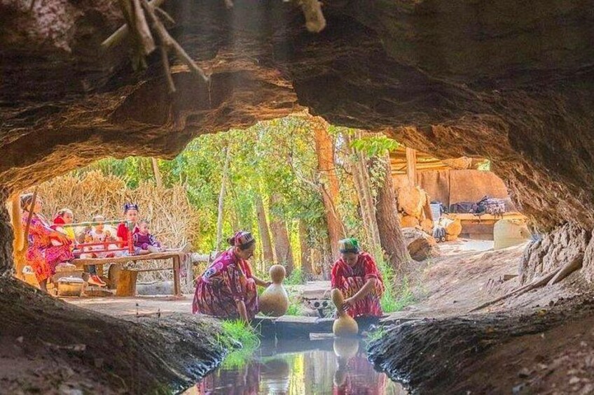 Eine unterirdische Höhle mit Menschen, die traditionelle Aktivitäten ausüben, einer Holzkonstruktion und einem natürlichen Wasserspeicher. 1