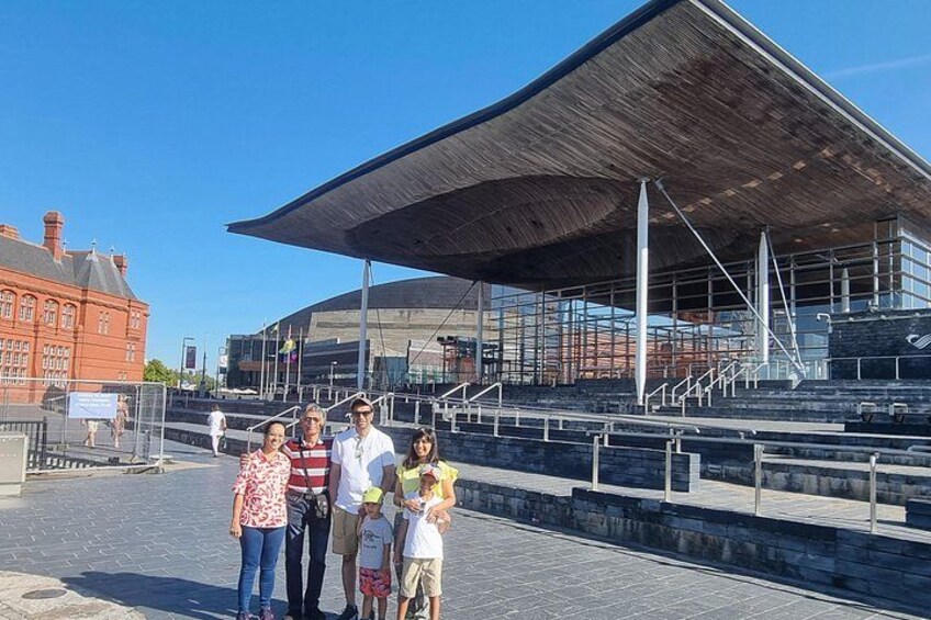 A group of people standing in front of a modern architectural structure with a large overhang and a staircase leading up to it. 4