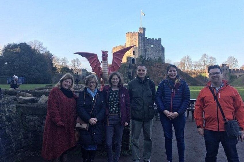 A group of people standing in front of a castle with a dragon statue. 2
