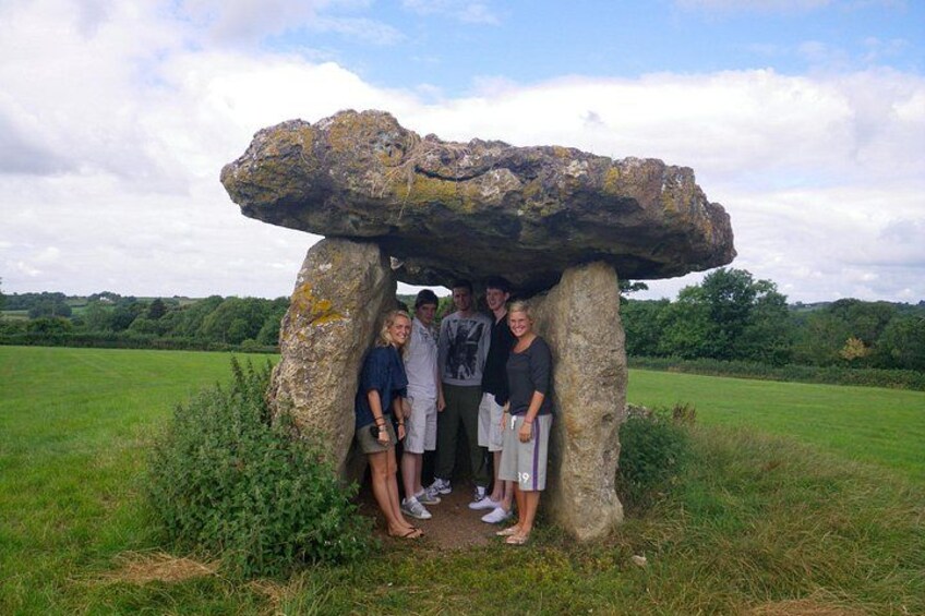 A group of people standing under a large stone structure in a grassy field. 5