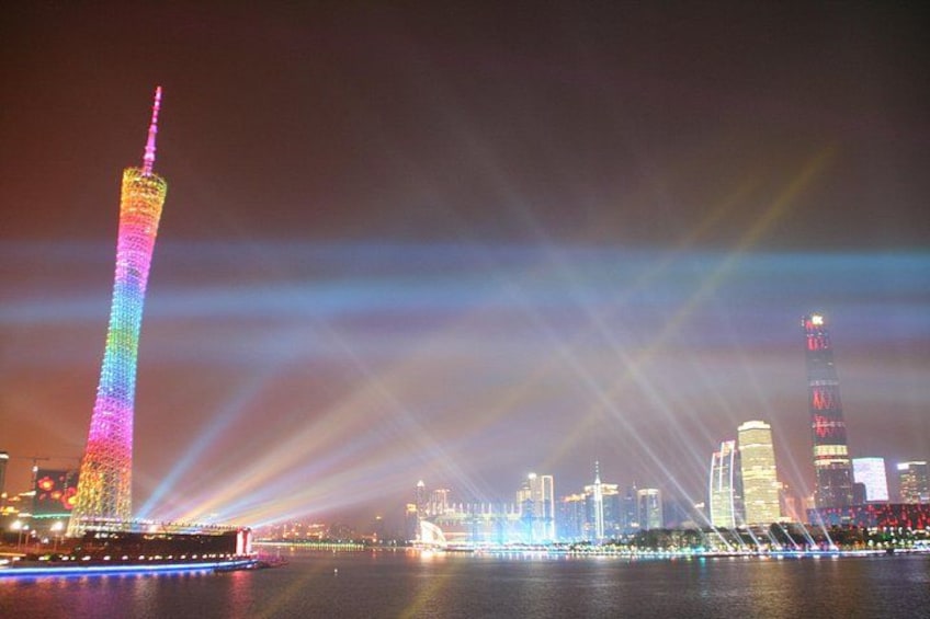 A brightly lit tower with a rainbow color pattern, a city skyline with illuminated buildings, and a body of water reflecting the lights. 1