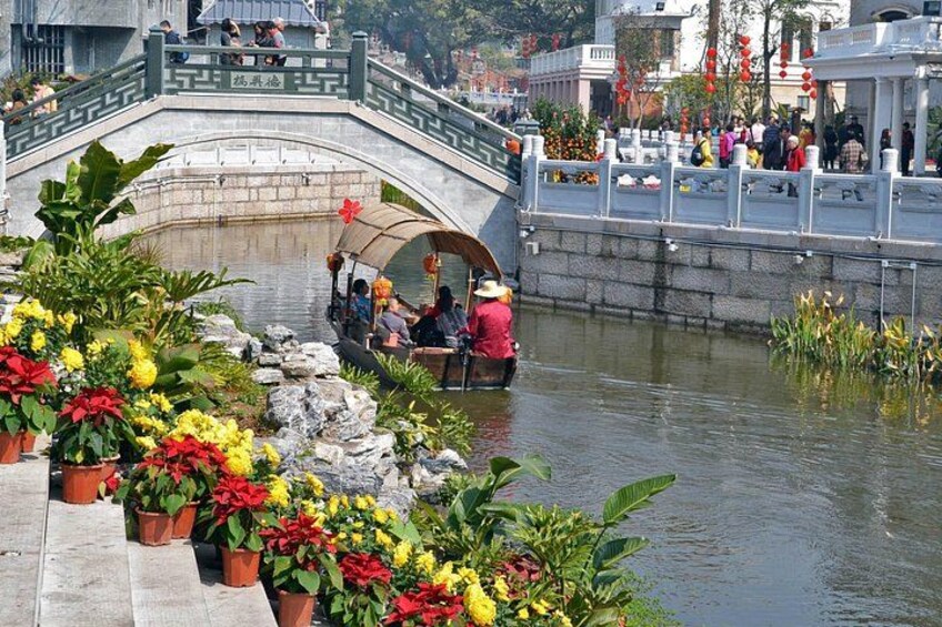 A stone bridge over a river with people on a boat and colorful flowers in the foreground. 4