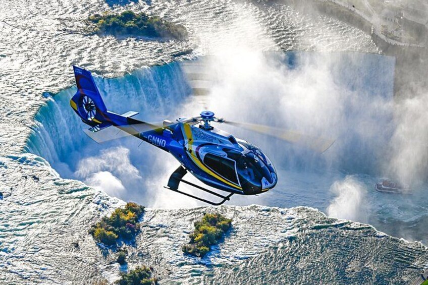 Een blauwe helikopter vliegt boven een waterval. 1
