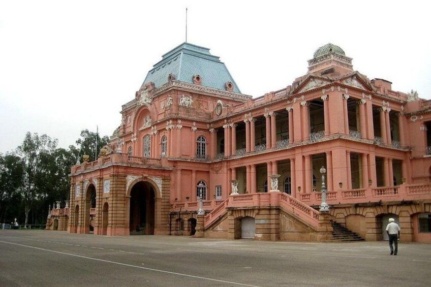 A large pink building with a dome and columns, a staircase, and a person walking in front. 1