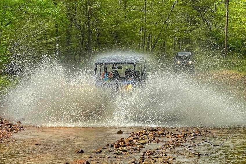 A vehicle driving through a shallow water crossing, creating a spray of water. 2