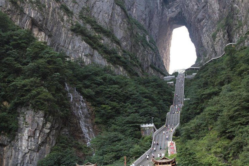A road winding through a mountainous area with a large rock formation and a waterfall. 2
