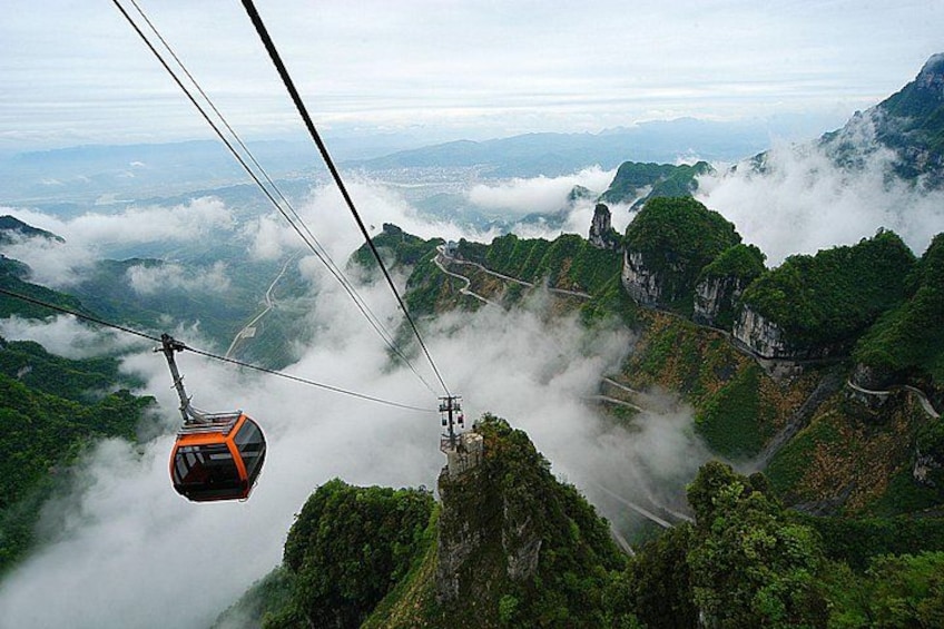 A cable car suspended over a mountainous landscape with lush greenery and mist-covered peaks. 1