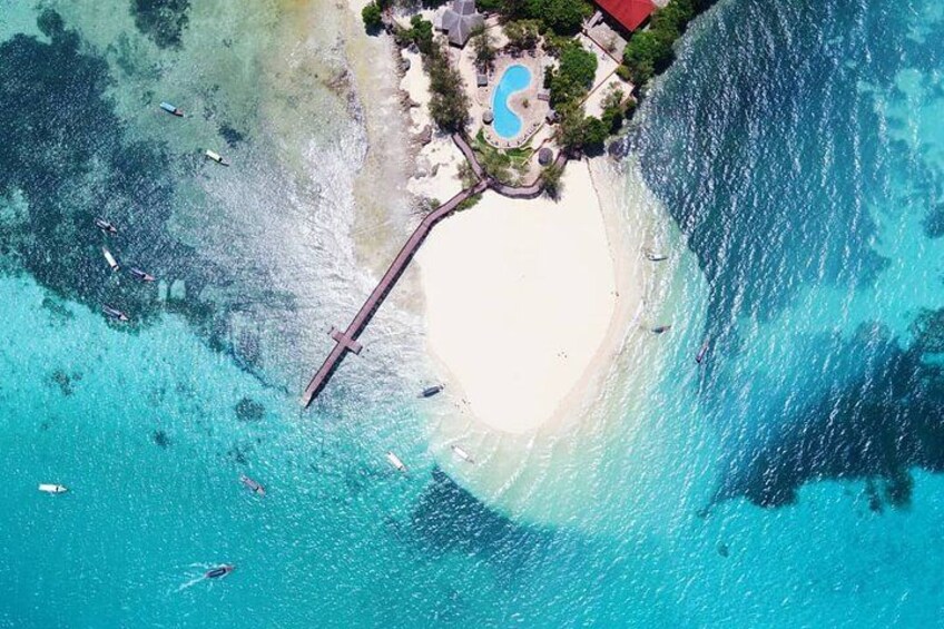 Ein Strand mit klarem türkisblauem Wasser, einem weißen Sandstrand und einem kleinen Pool. 2