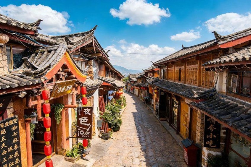 Una calle estrecha bordeada por edificios tradicionales de madera, faroles rojos y un cielo azul despejado. 1