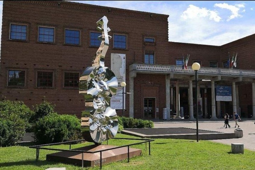 Una escultura frente a un edificio de ladrillo con columnas y banderas. 4