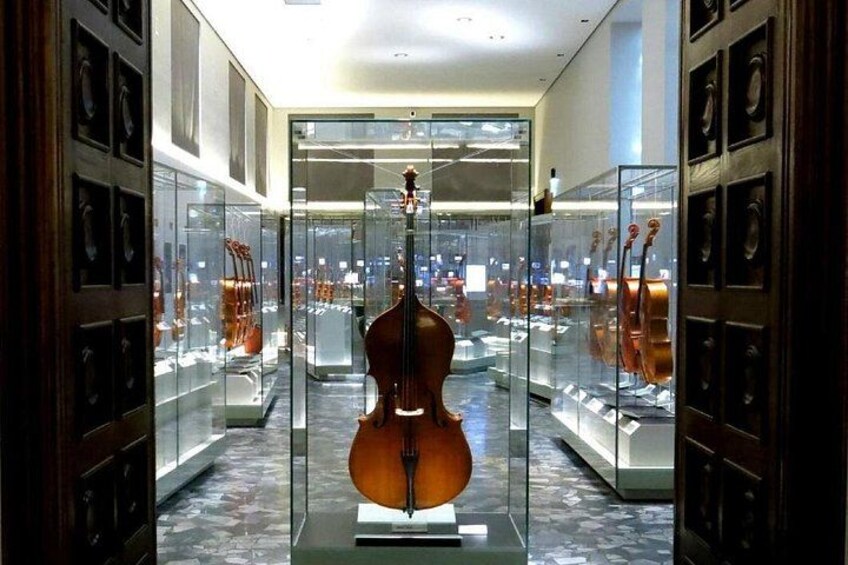 Una vitrina de vidrio con un violonchelo en el centro, rodeado de otros instrumentos musicales. 1