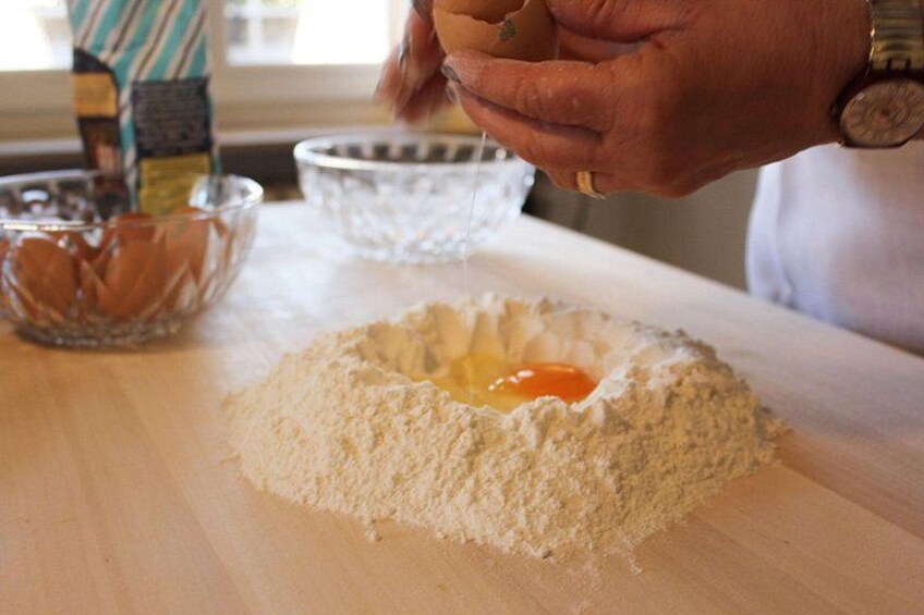 A person cracking an egg into a flour mound on a wooden surface. 2
