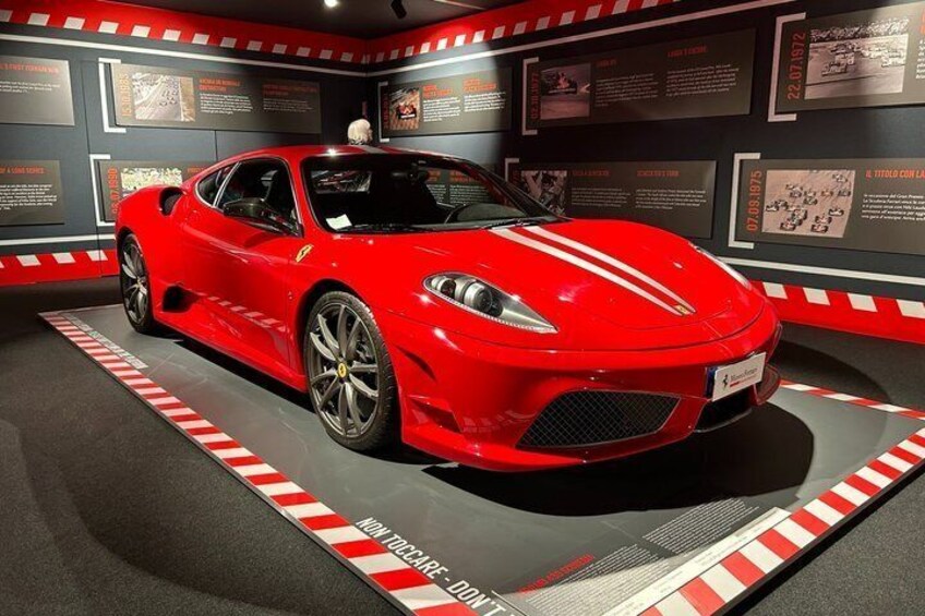 Un coche deportivo rojo en una exhibición de museo, con paneles informativos y un suelo a rayas. 3